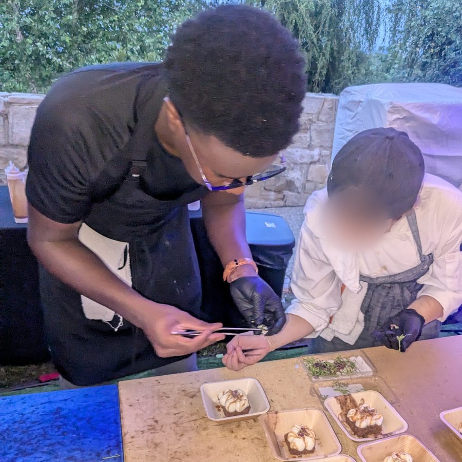 Ace finishing desserts with tweezers alongside another cook