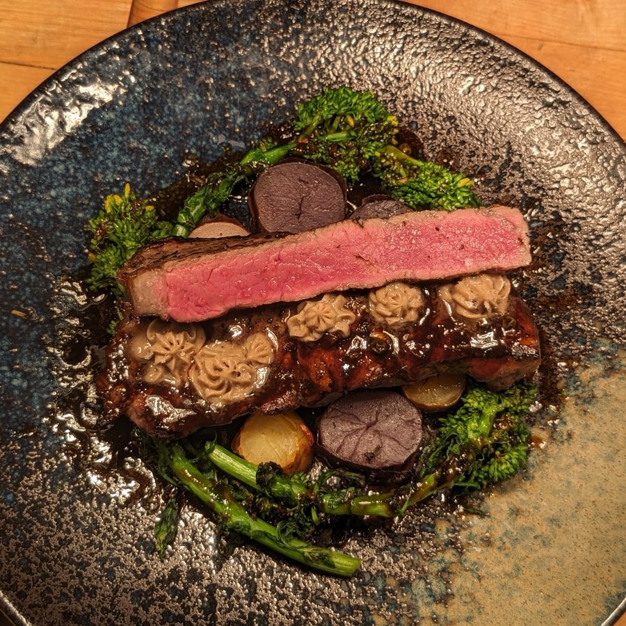 Sliced steak over broccolini and fingerling potatoes with piped butter