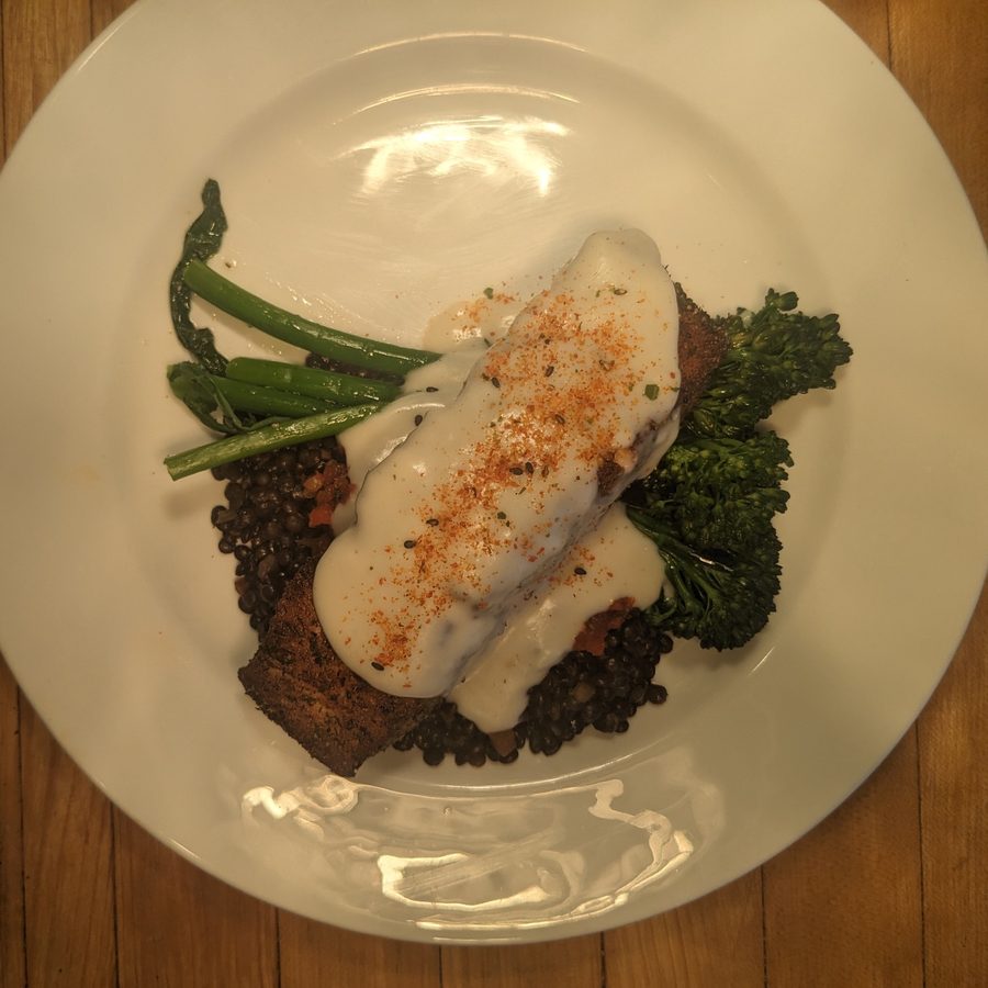 Crusted fish with white sauce over black lentils and broccolini