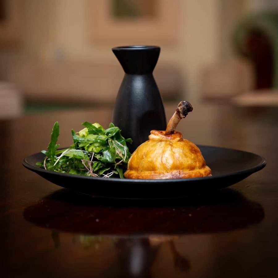 Golden pastry-wrapped chicken leg with a dressed green salad on a black plate